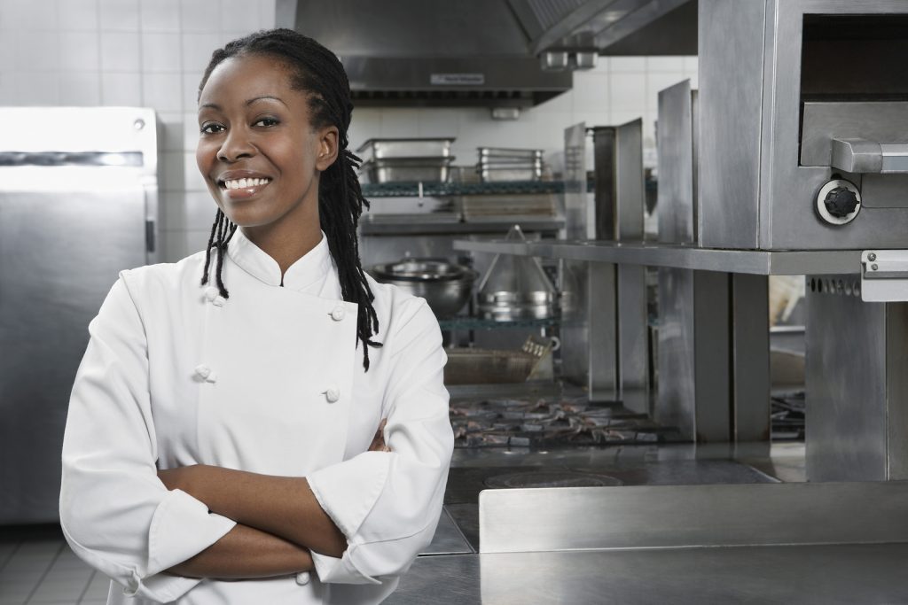 Portrait of a smiling female chef with hands crossed in the kitc