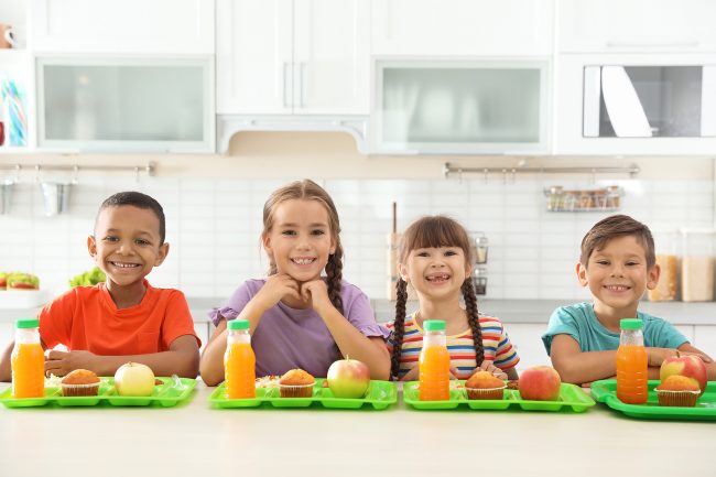 Children sitting at table and eating healthy food during break at school