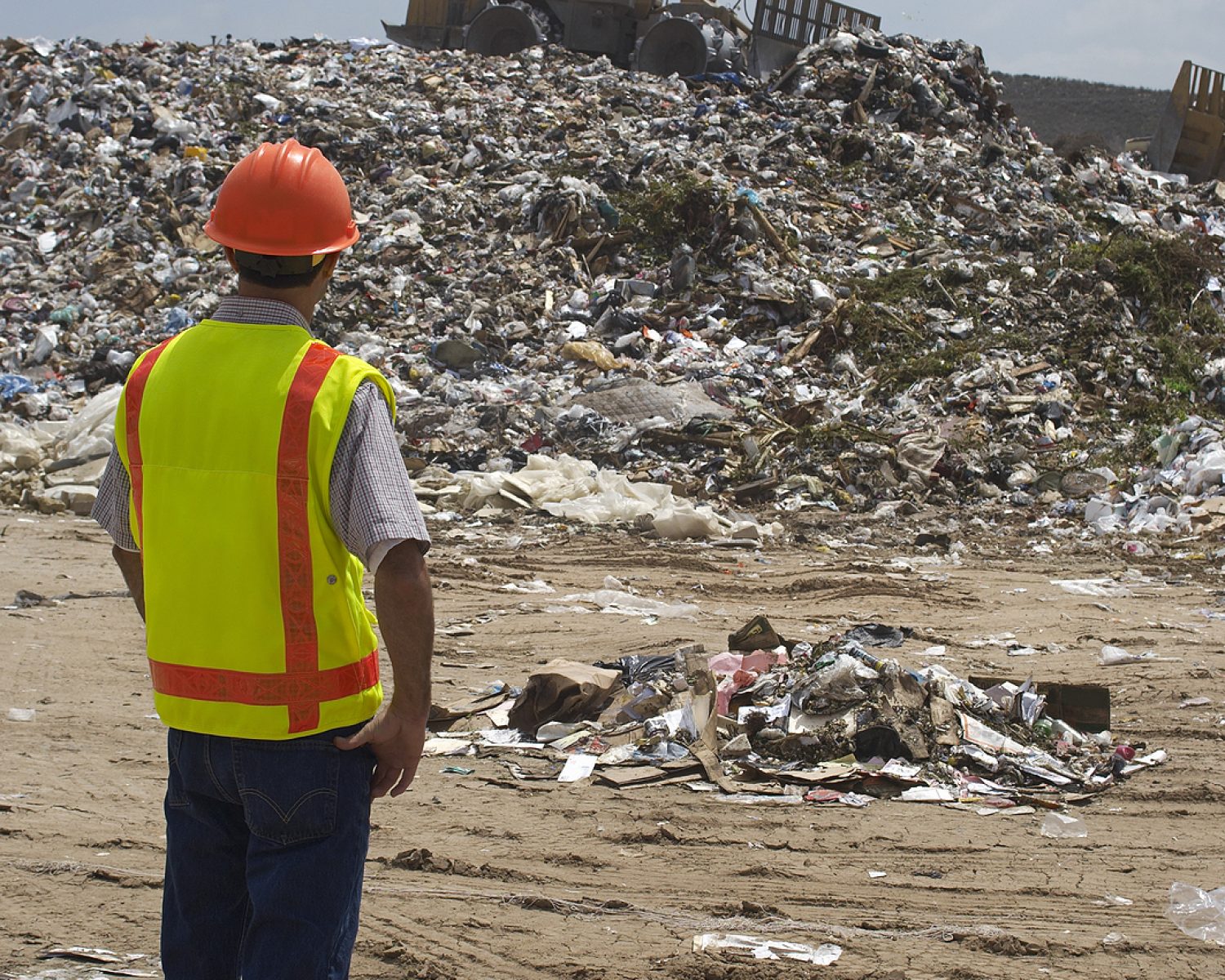 Worker watching digger moving waste at landfill site